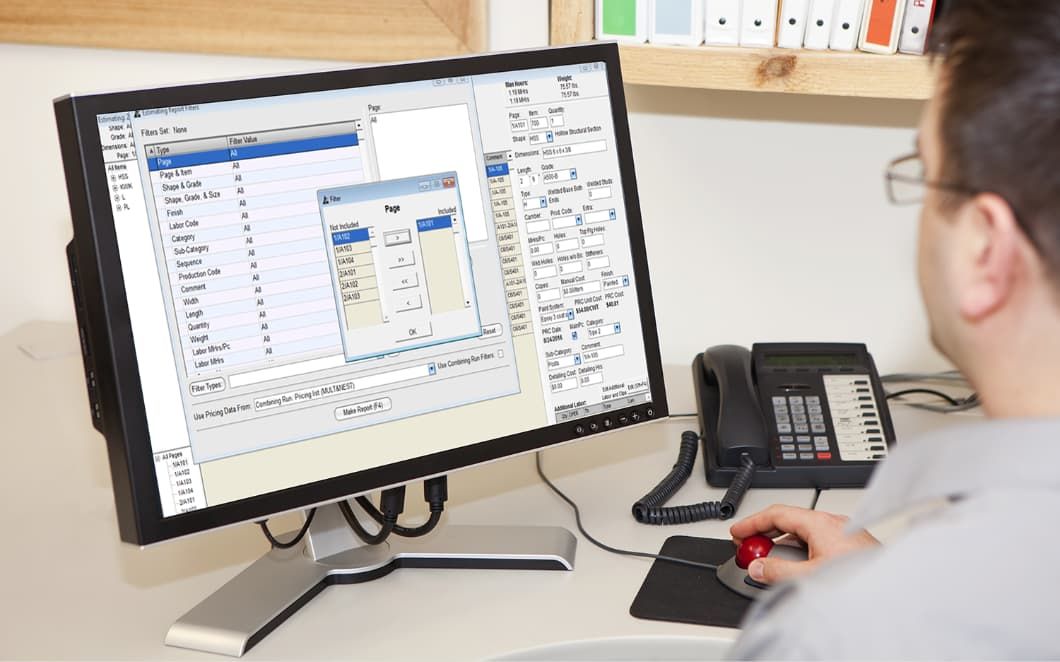 A man in glasses is sitting at a desk and looking at a computer screen where he is using a reporting software.