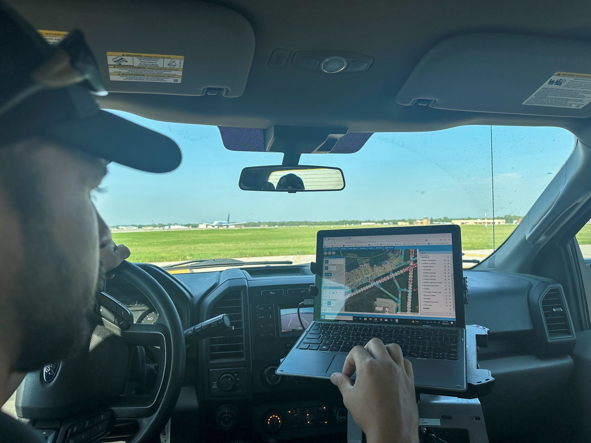A person in a truck uses a laptop to view a map and data, likely for field operations.