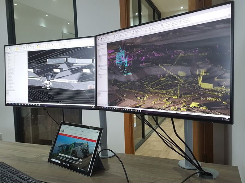 Dual monitors display 3D modeling and point cloud data of construction projects.