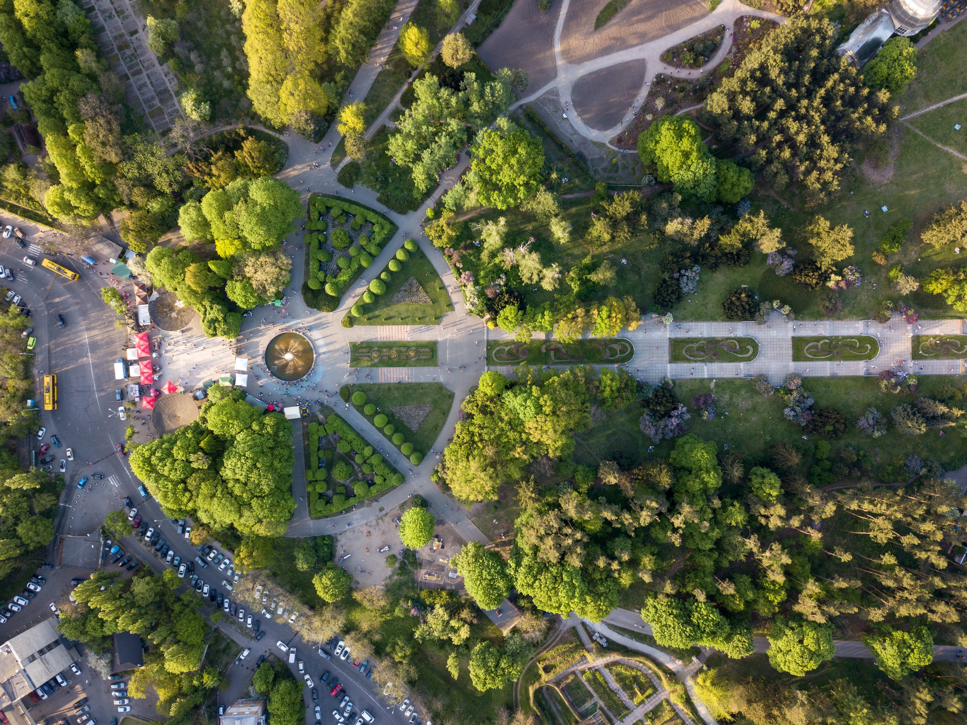 Aerial view of a park with geometric gardens, a fountain, and surrounding trees.