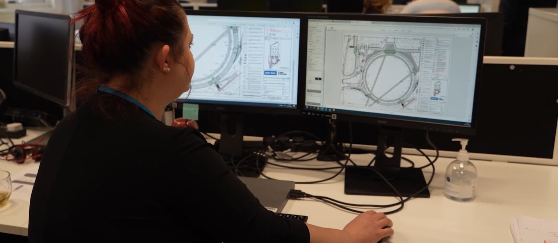 Engineer reviewing technical designs on dual monitors at a desk.