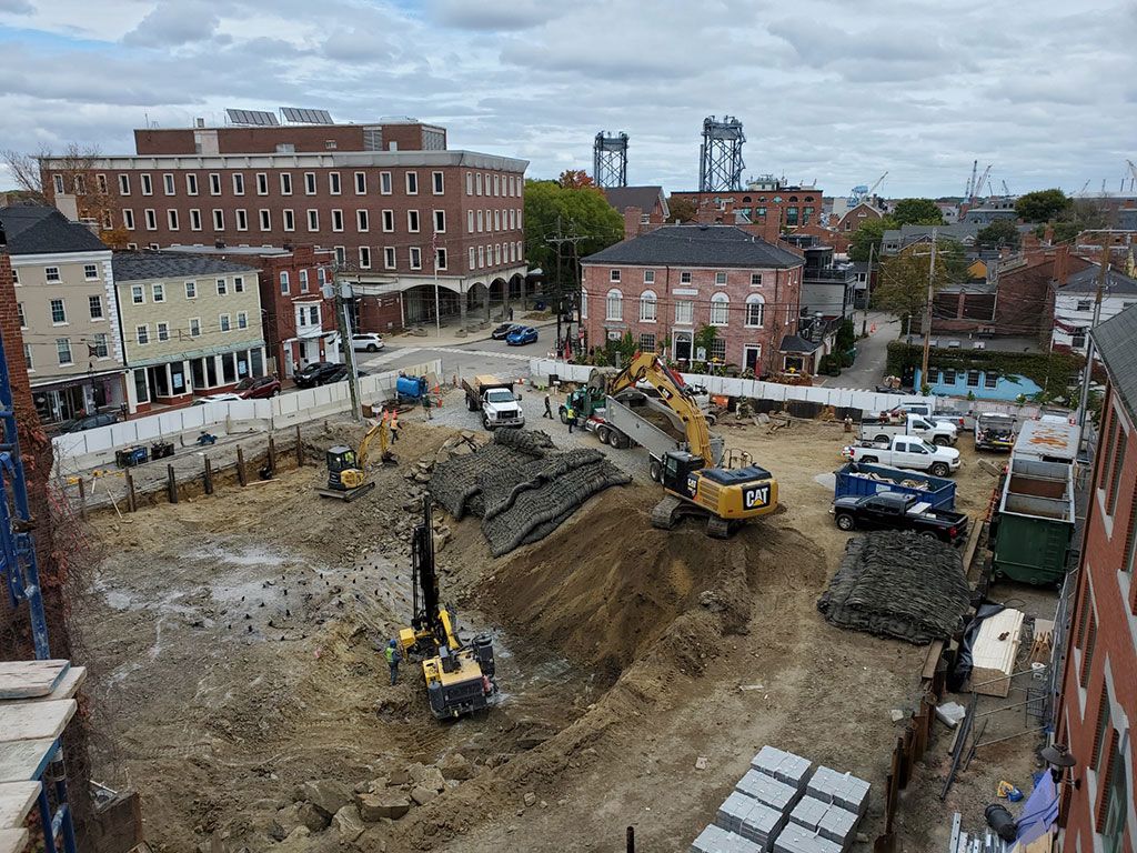 Construction site with excavators, trucks, and buildings in the background.