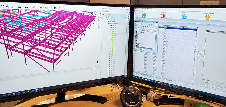 Two monitors display architectural designs, one has a 3D model of a pink and blue steel building structure and the other showing data tables & graphs.