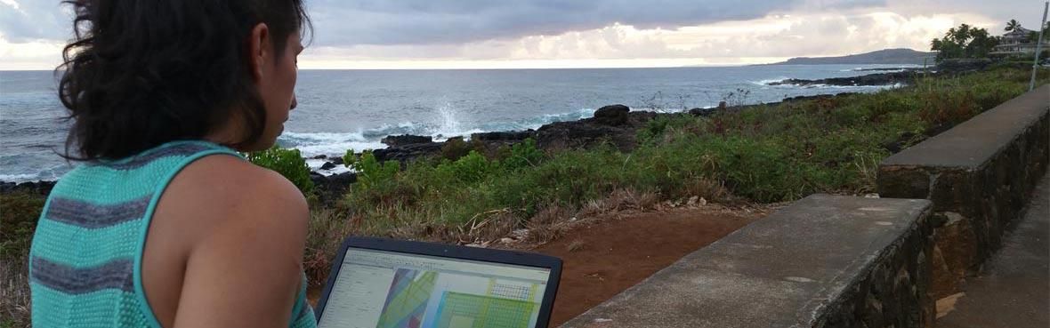 A woman sits outside with a laptop overlooking the ocean on a cloudy day.
