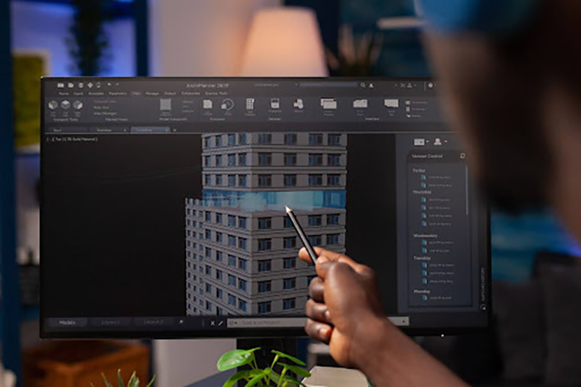 A person's hand is shown using a stylus to interact with a 3D model of a building on a computer screen.
