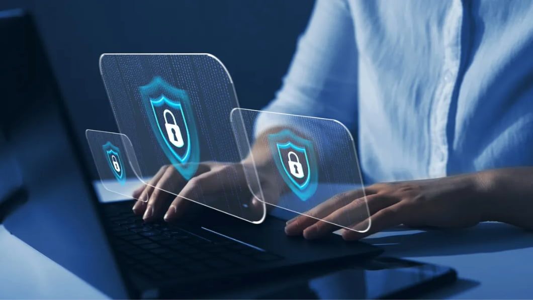 Hands typing on a laptop with glowing blue shield and lock icons representing digital data protection.