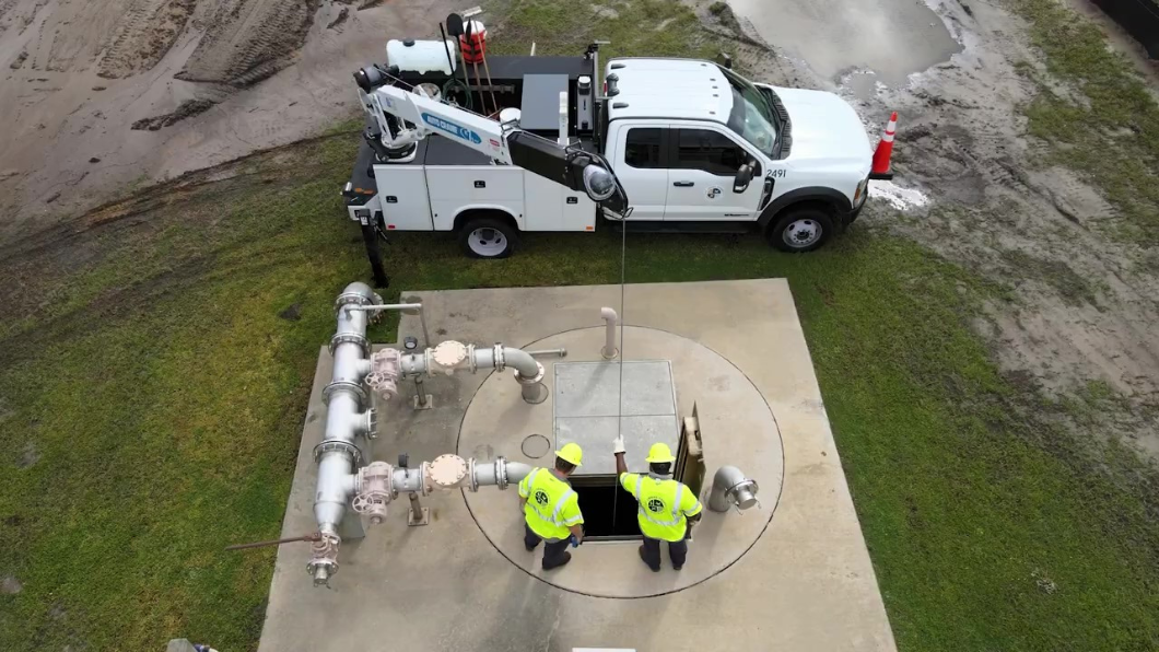 Two utility workers wearing hardhats and safety vests inspect wastewater treatment infrastructure after a rainstorm in St. Johns County, Florida.