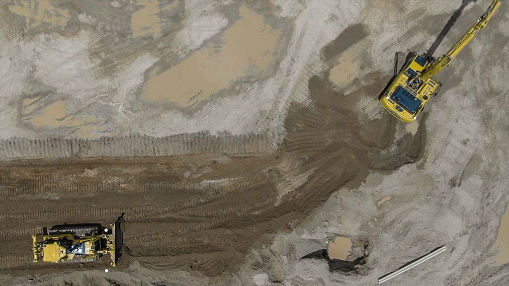 Aerial view of a construction site with a yellow excavator and bulldozer on muddy ground.
