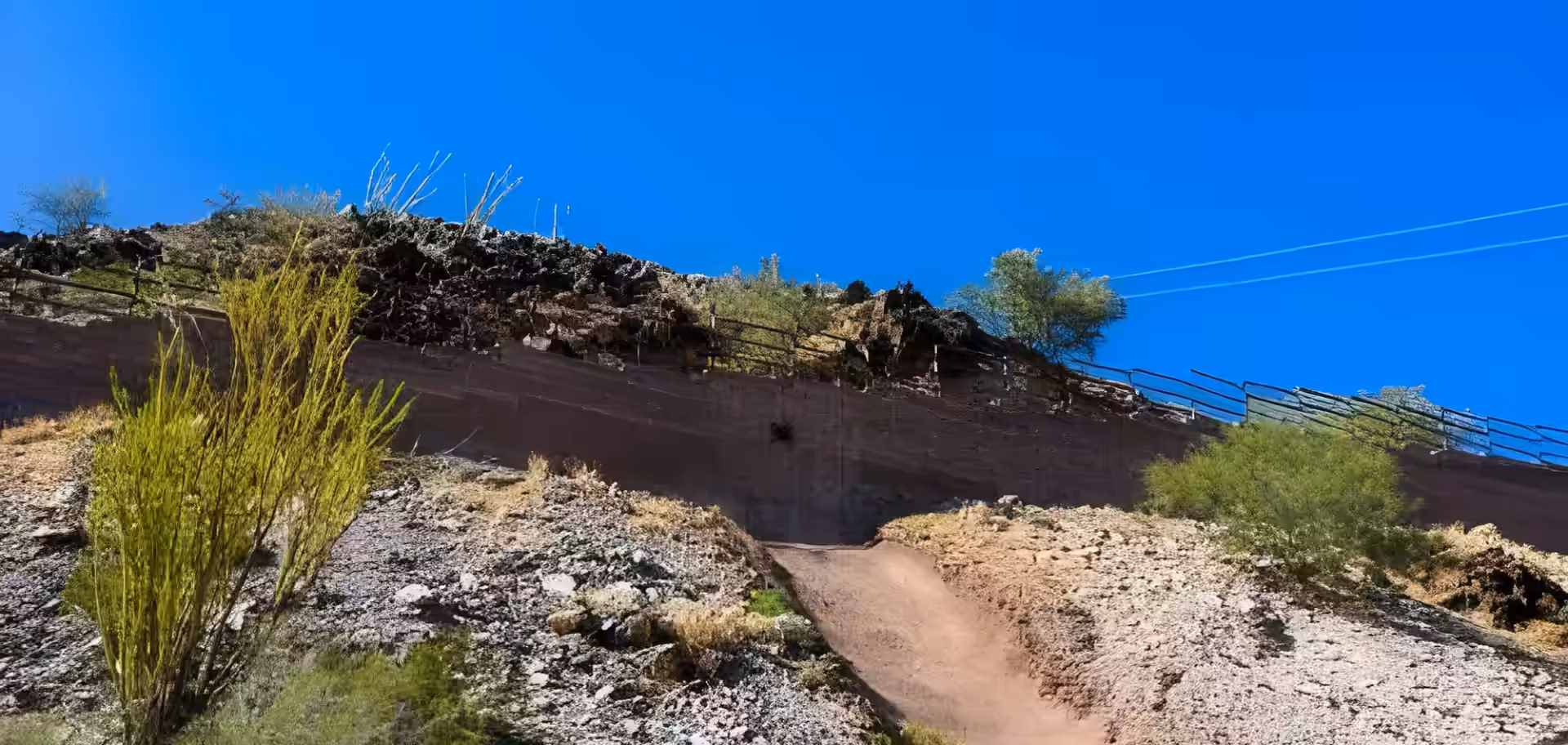 View from the base of a steep, rocky slope on North Mountain, showing a dirt trail leading up to a reinforced retaining wall.