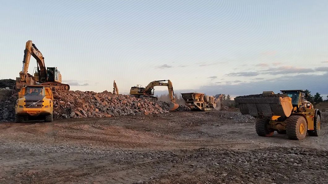 Heavy construction site with excavators, a dump truck, and a wheel loader moving rock piles at dusk.