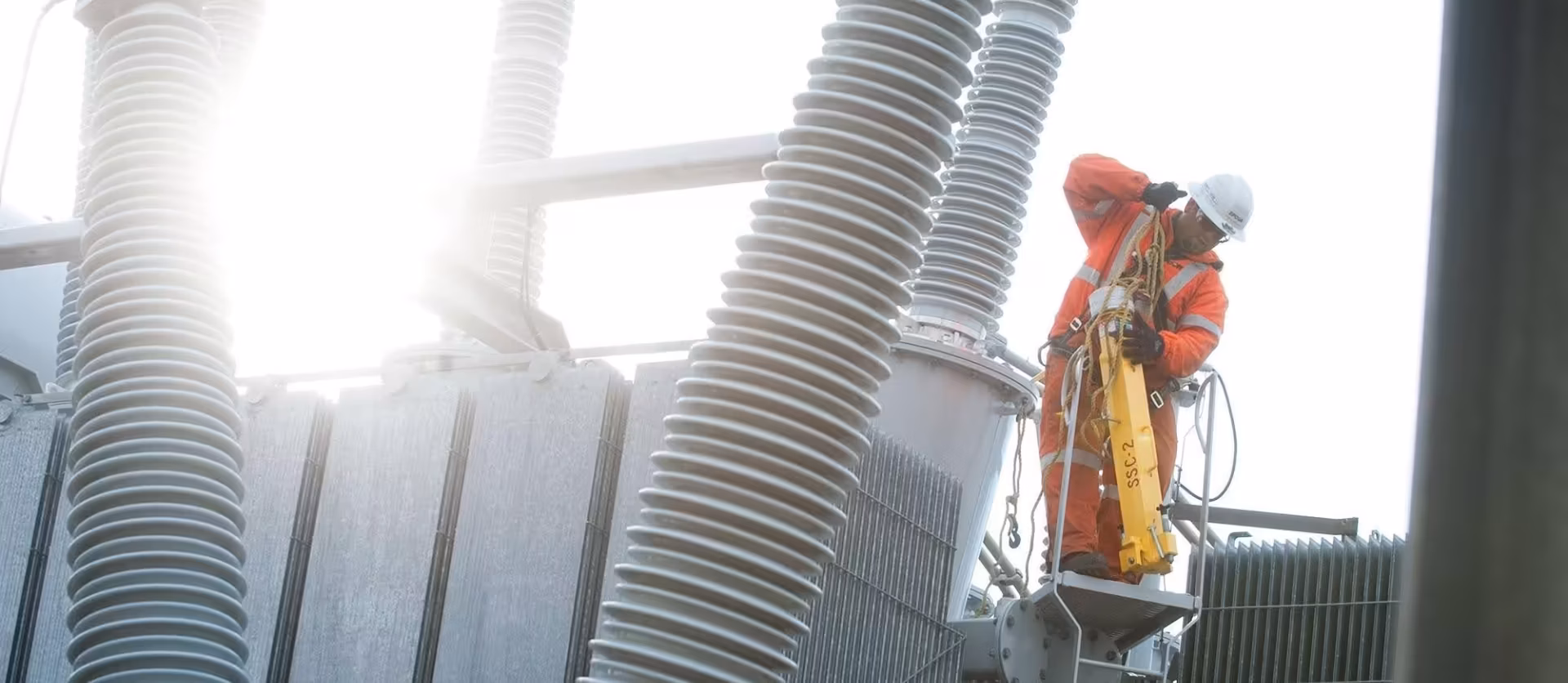 An EPCOR utility worker in high-visibility gear performing maintenance on high-voltage substation insulators.