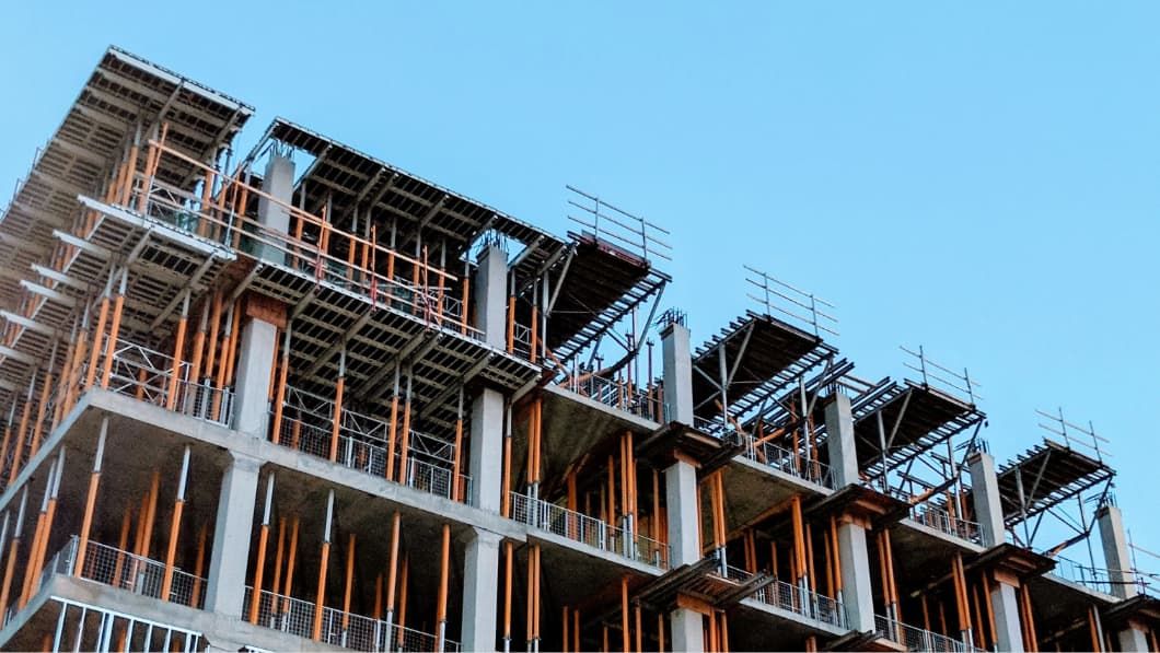 A multi-story building under construction with concrete floors and pillars, metal framing for windows and wooden scaffolding