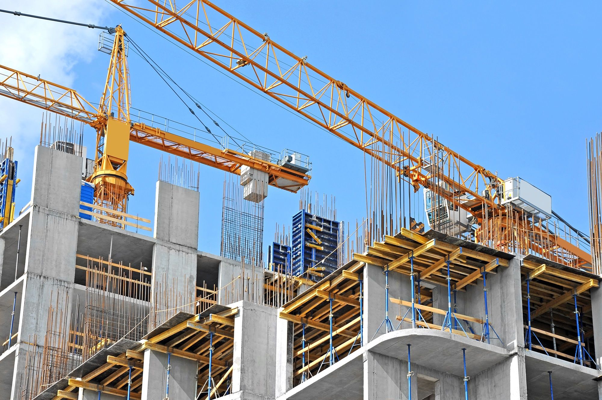 Construction crane over a building under construction with concrete framework against a blue sky.