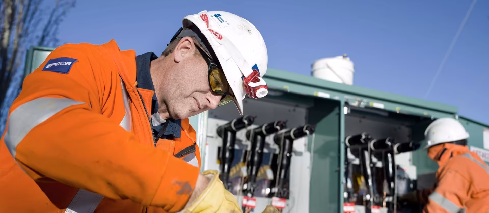 Close-up of an EPCOR technician in a hard hat and safety glasses inspecting electrical transformer components.