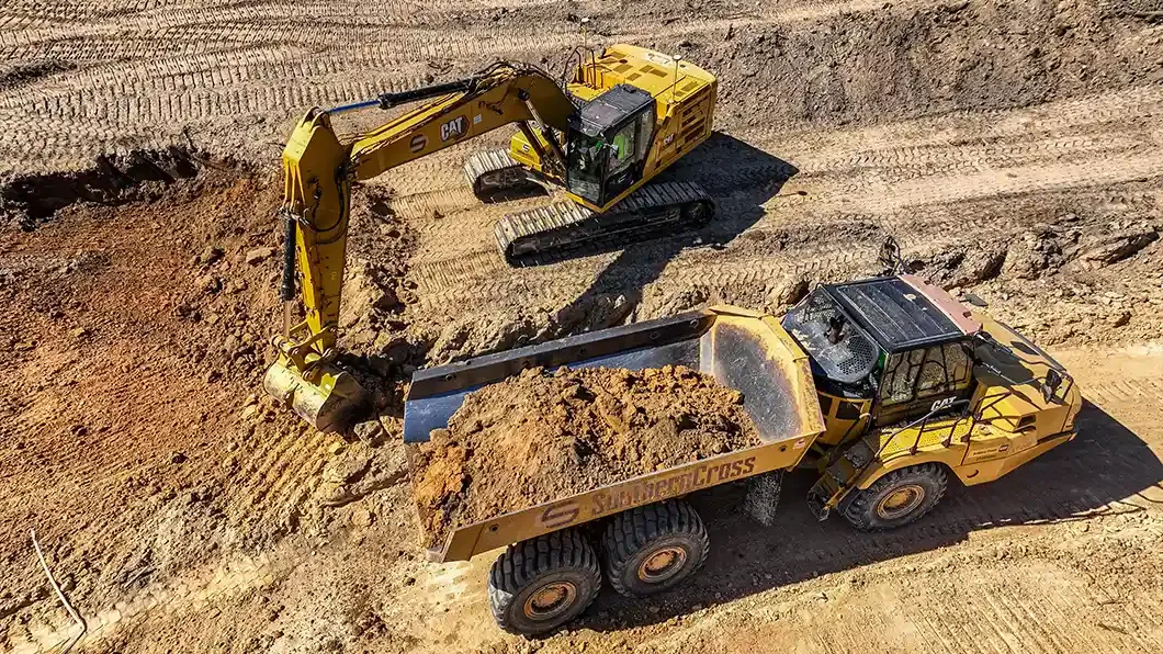 Aerial view of an excavator loading dirt into an articulated dump truck on a dirt jobsite.