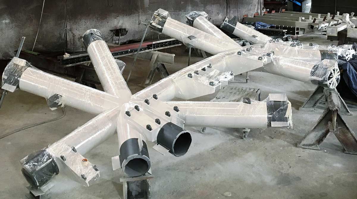 A star-shaped assembly of white pipes, some wrapped in plastic, rests on a shop floor.