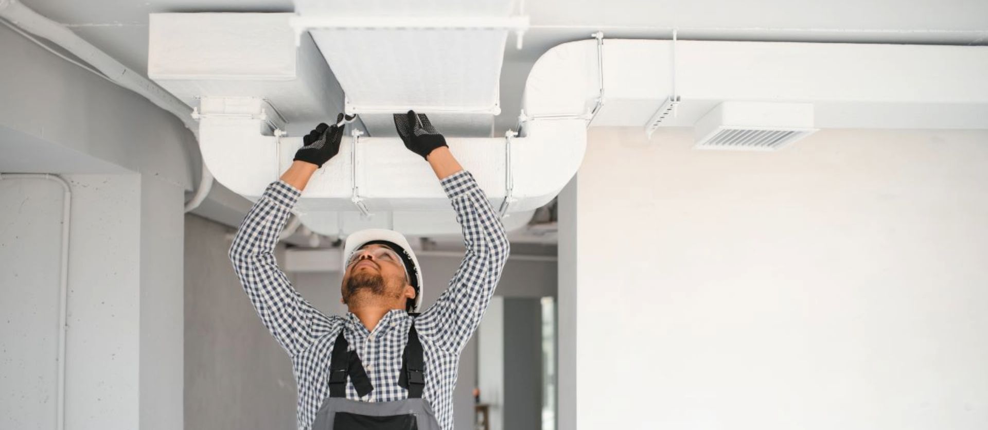 Worker in overalls installing ceiling ventilation system in a modern interior space