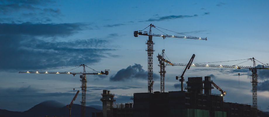 A silhouette of a construction site with multiple cranes against a twilight sky.