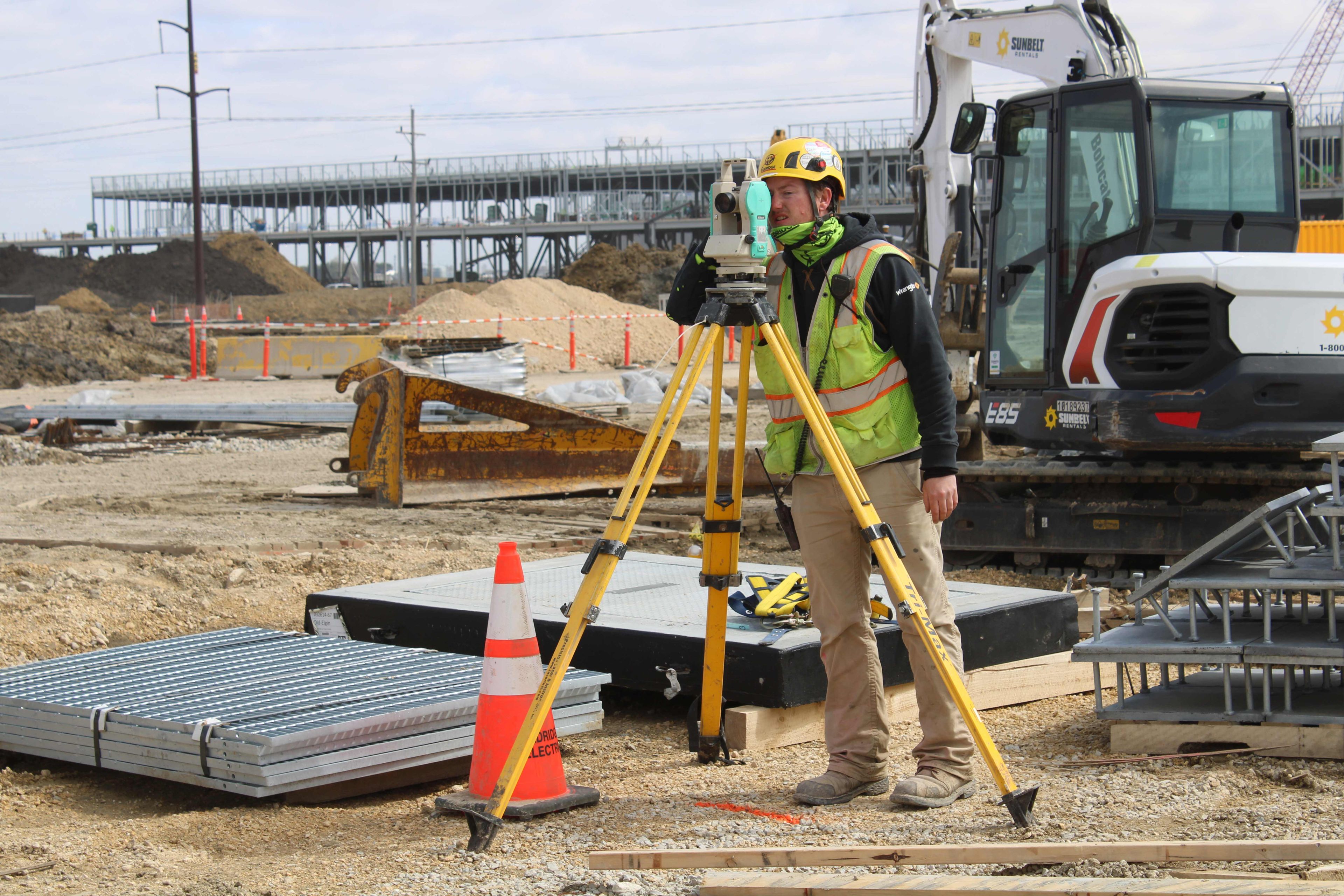 Surveyor using a total station with a construction site in the background.
