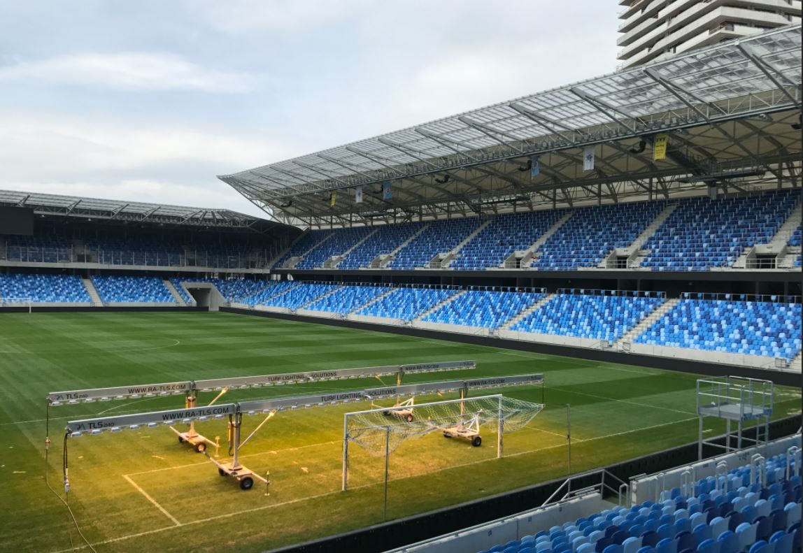 Empty stadium with blue seating and portable lights on the field.