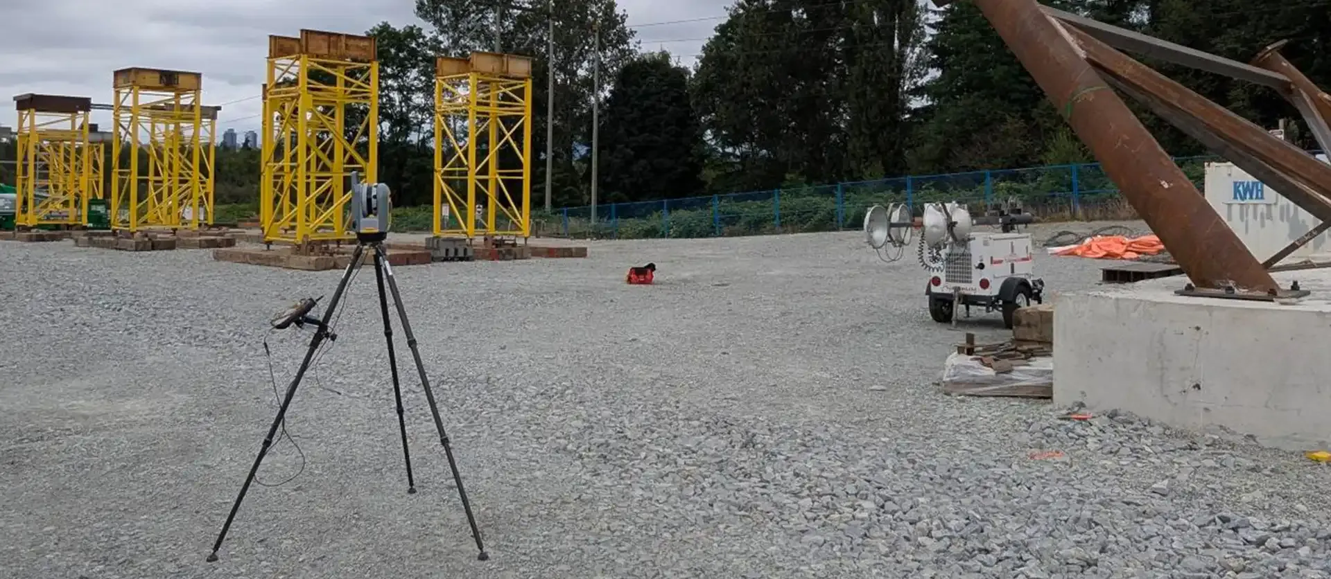 A Trimble total station pointing towards a section of steel structural supports on a construction site.