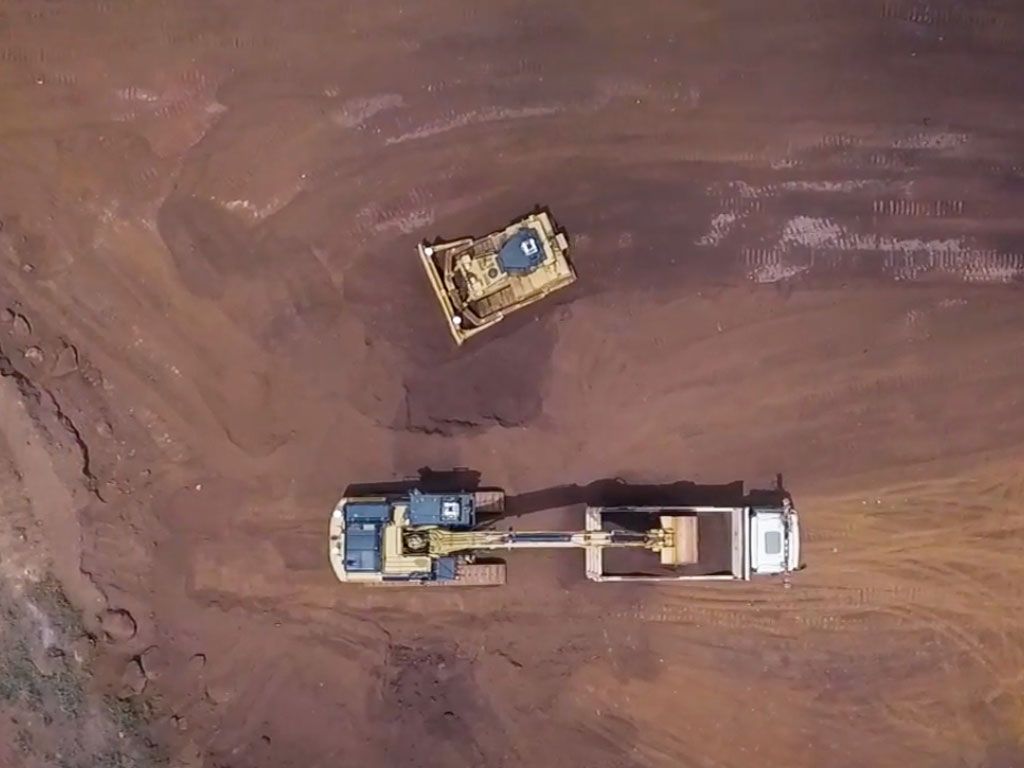Aerial view of heavy machinery, including an excavator loading a dump truck and a bulldozer, on a construction site.