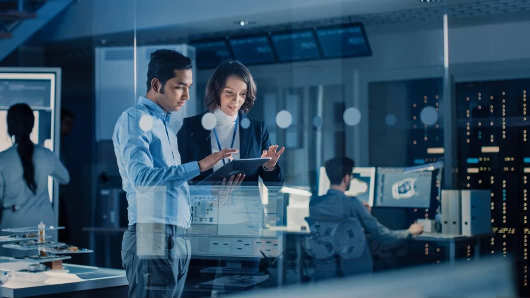 Diverse colleagues collaborating on a digital tablet in a high-tech, blue-lit server room.