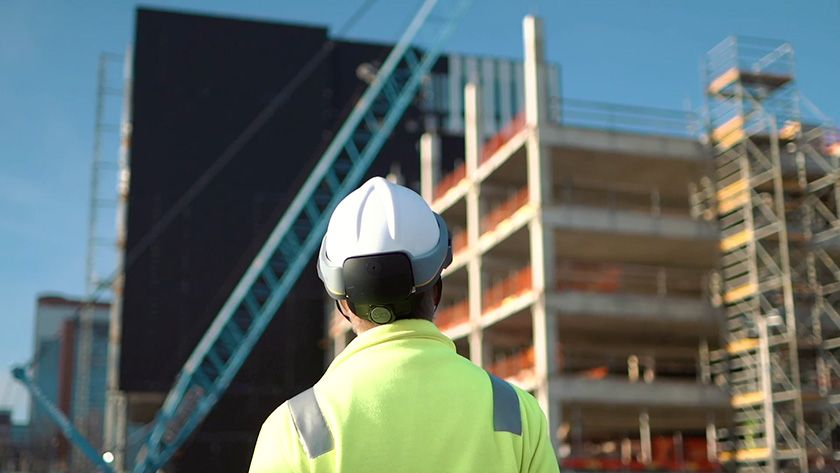 A construction worker in a hard hat and high-visibility vest looks at a building under construction.