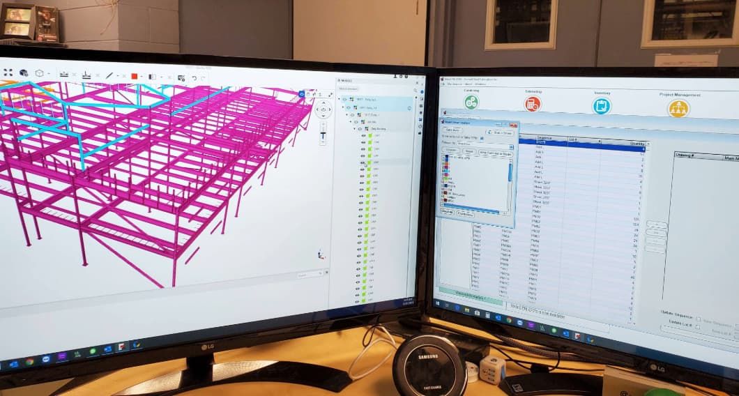 Dual-screens with architectural design software. The left screen has a 3D rendering of a building's steel frame and the right, project management data
