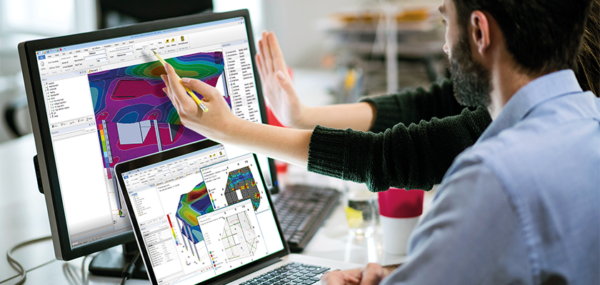 Man sat facing computer and laptop, monitors show slab deflections in Tekla Structural Designer