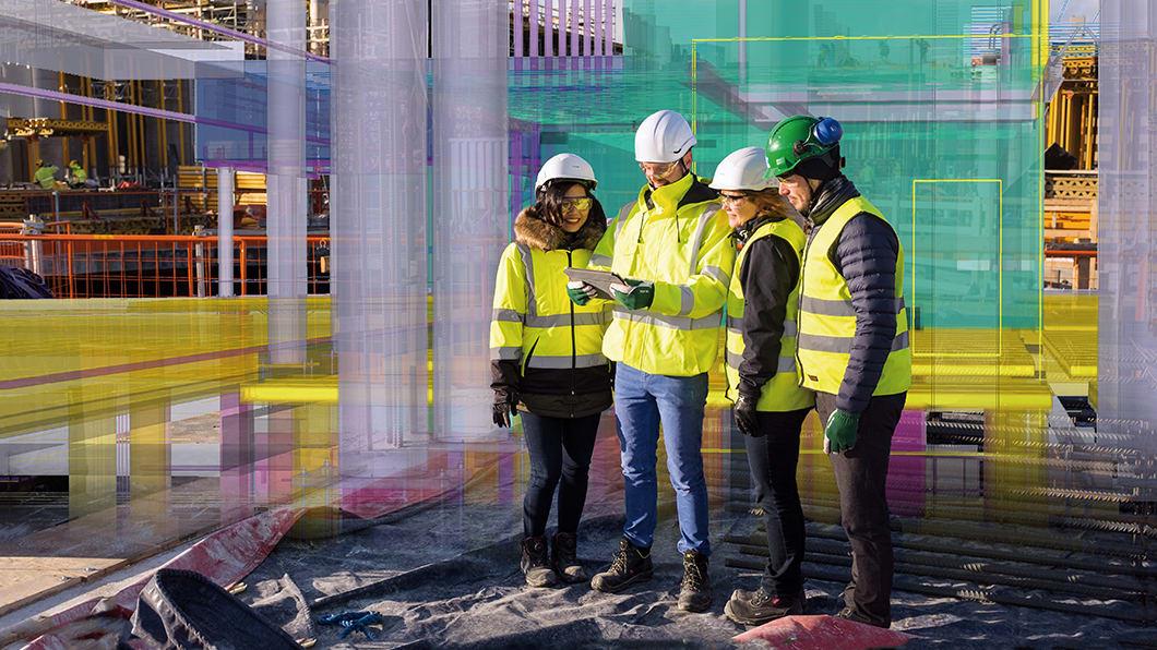 4 construction professionals wearing safety gear and high-visibility jackets examine a tablet on a construction site