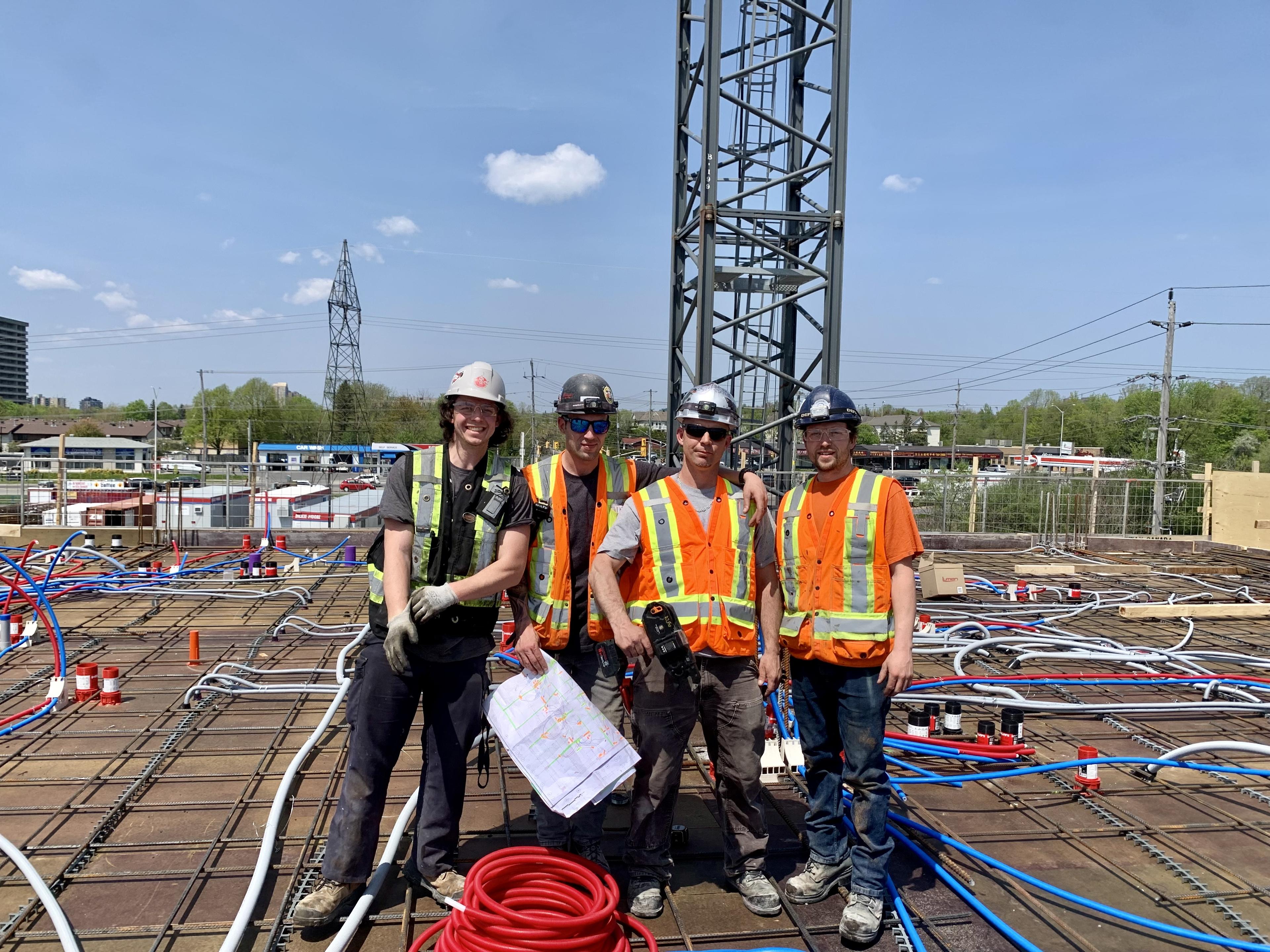 Three people in hard hats and hi-vis safety clothing pose for a picture on the roof of an action construction site.