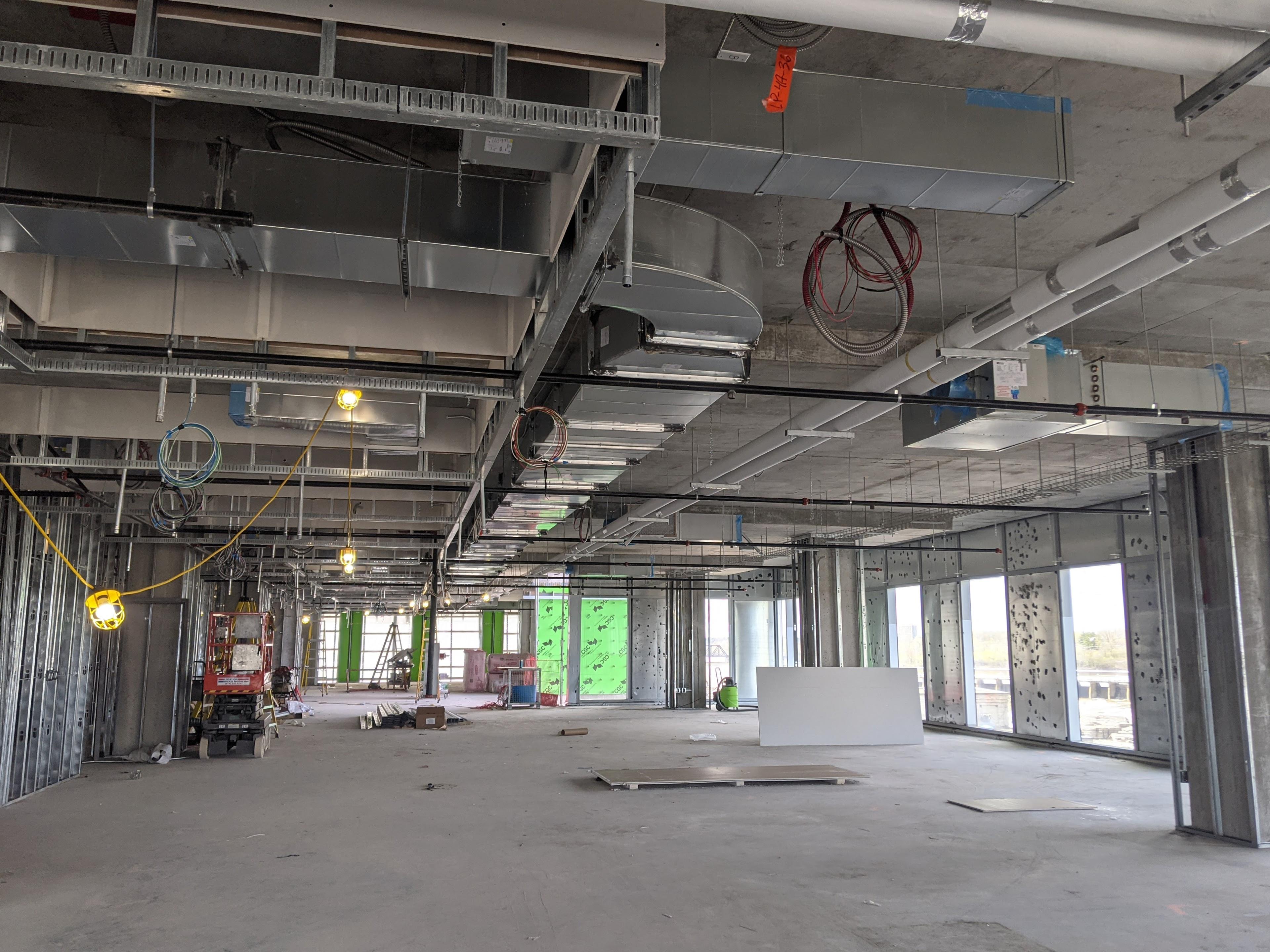 An open room in a construction site shows an open ceiling with visible in-progress electrical and HVAC