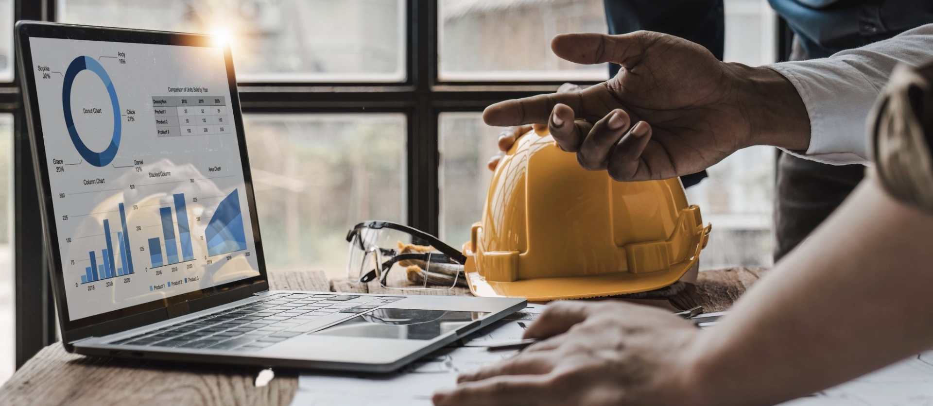 Laptop showing charts, hard hat, and hands discussing construction data