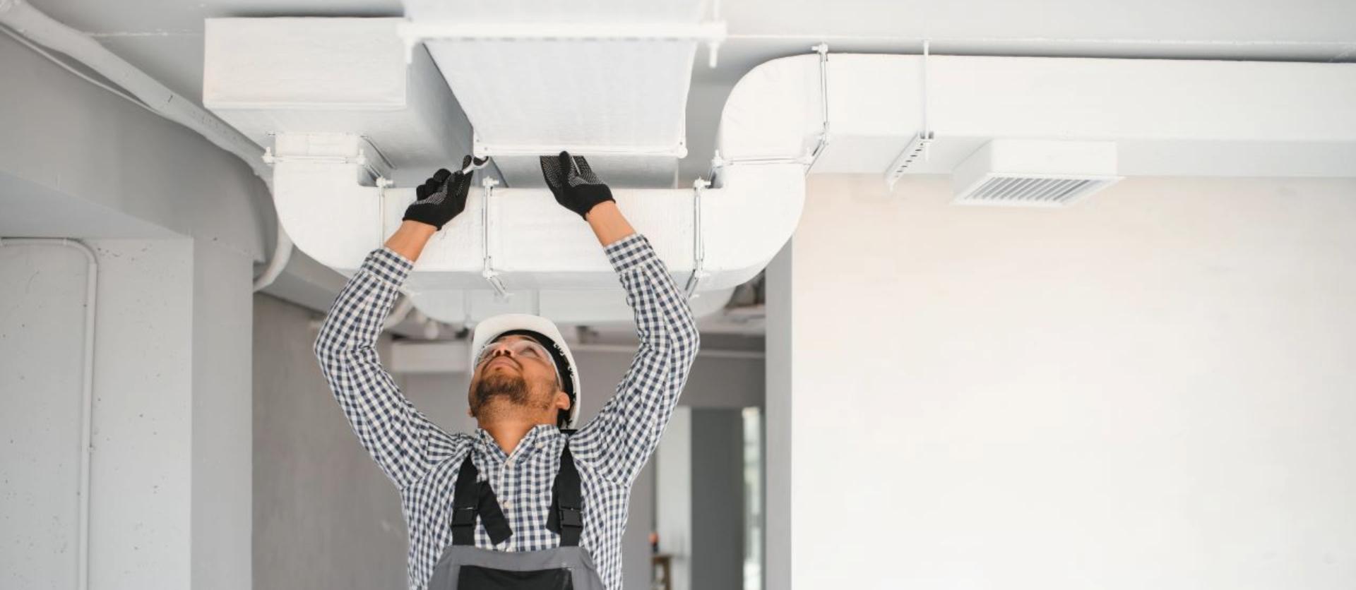 Worker in overalls installing ceiling ventilation system in a modern interior space