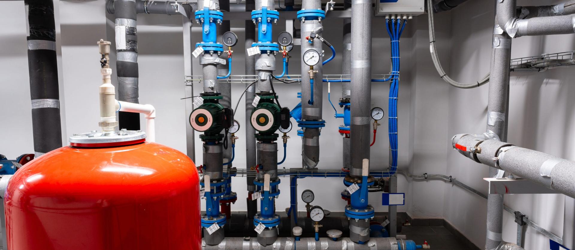 Boiler room with red tank and insulated pipes with gauges