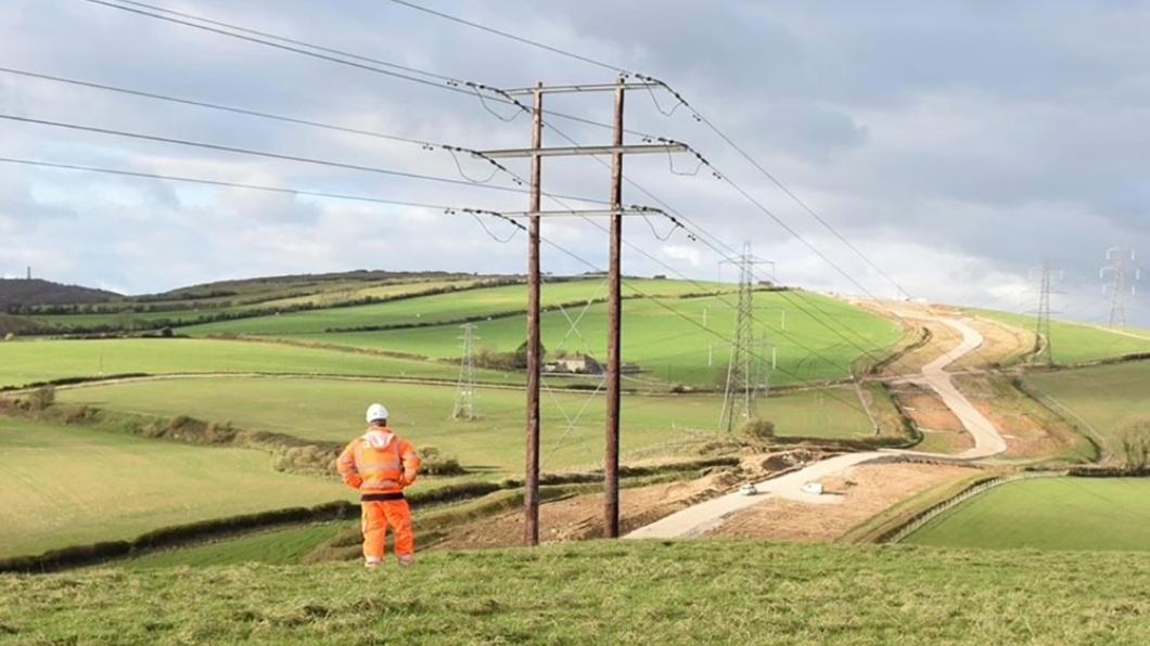 Construction worker looking at overhead power towers in a field