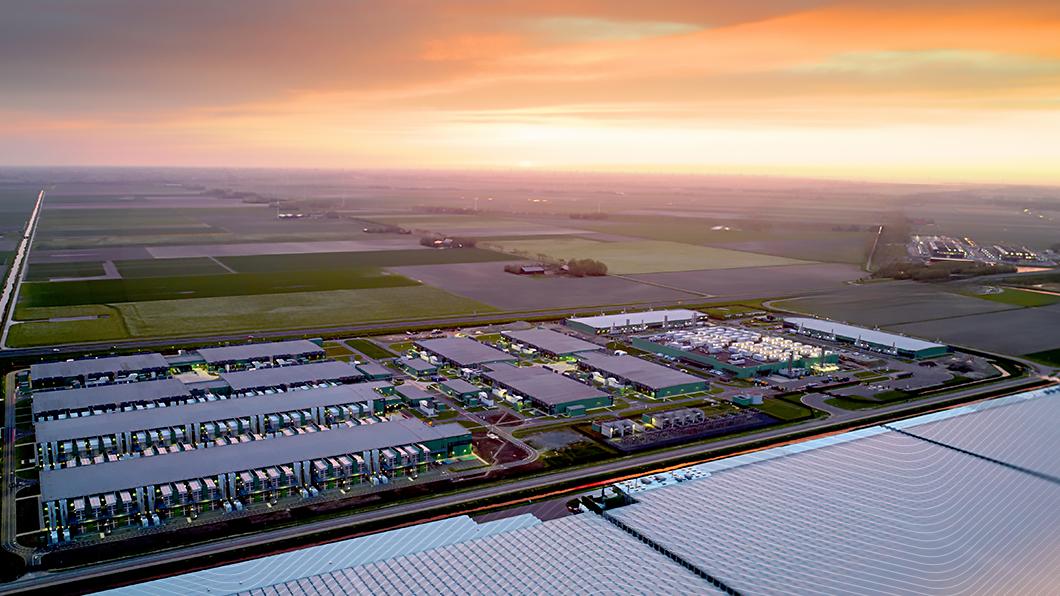 Aerial view of a large data center surrounded by fields at sunset, with vibrant orange and pink sky.