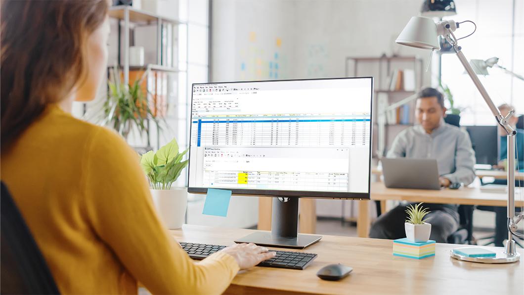 Woman working on a computer in a modern office setting with plants and desks.